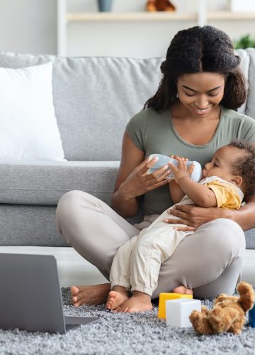 Maternity Leave Concept. Young Black Mother Giving Bottle With Water To Baby