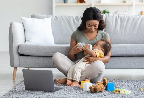 Maternity Leave Concept. Young Black Mother Giving Bottle With Water To Baby