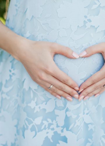 Pregnant woman in light blue dress holding her pregnant belly and love sign - maternity concept